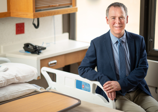 Dr. Loren Denlinger in a jacket and tie by a bed at University Hospital