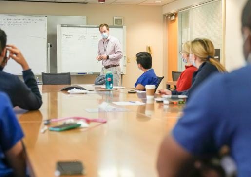 Dr. Andy Coyle in front of a white board lecturing to internal medicine residents seated a conference room table