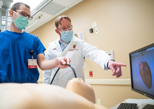 Dr. Steven Ewer points at a heart image on a monitor while a fellow works with a manikin in the UW Health Simulation Program