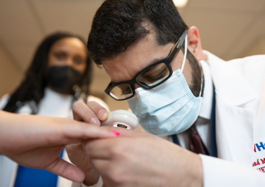 Rheumatology fellow Dr. Asadullah Mahmood examines a patient's hand while Dr. Sancia Ferguson oversees