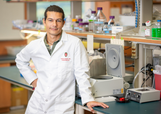 Dr. Andrea Galmozzi wearing white coat standing in front of lab bench