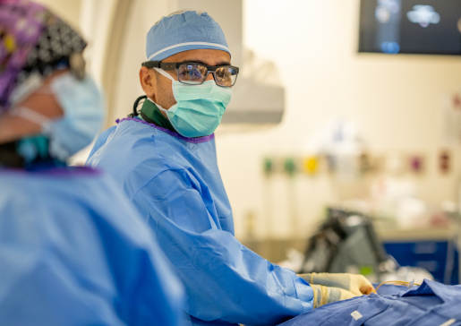 Dr. Farhan Raza wearing safety glasses and scrubs performing a procedure in the University Hospital cath lab