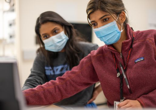 Closeup of two learners wearing masks leaning over computer screen