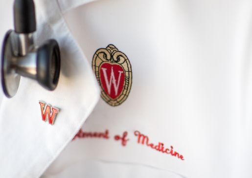Photo of a Department of Medicine white coat with embroidered University of Wisconsin crest in red and gold