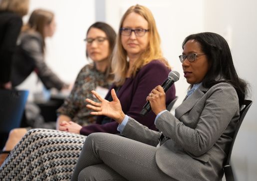 Dr. Christine Sharkey talks into a mic at a department event while Amy Zelenski and Allison Ishizaki look on