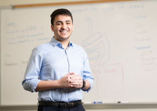 Dr. Mazen Almasry standing in front of a white board in a classroom, wearing a blue button down shirt and smiling..