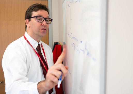Dr. Vasilevskis talking and gesturing in front of a whiteboard in a classroom