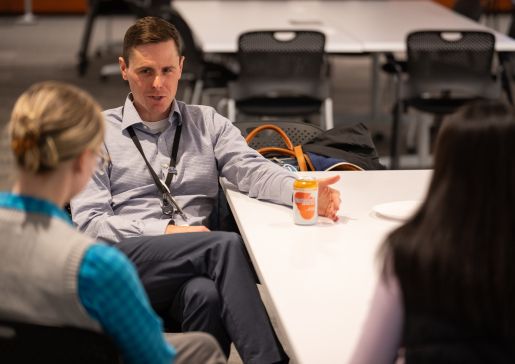 A man sitting at a table talking to two female students with their backs to the camera