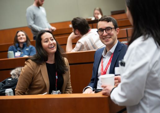 Several people sit in an auditorium, talking and smiling