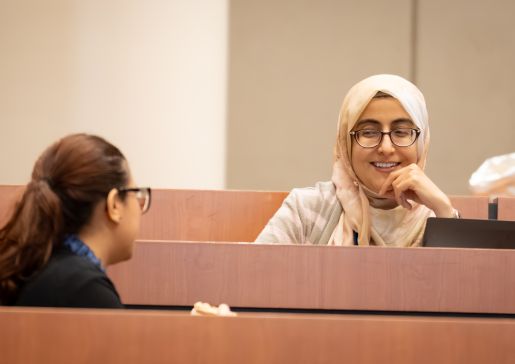 Two women talking to each other in seats in a lecture hall