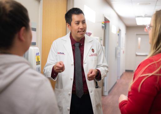 Dr. David Pham wearing a white coat talking with two female colleagues in the hallway of the Cardiovascular Medicine clinic